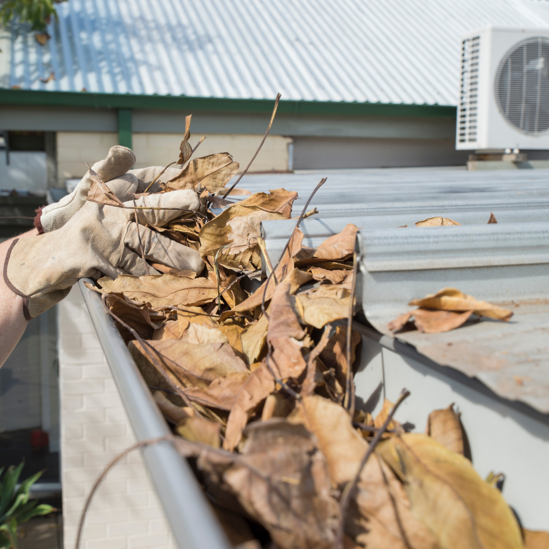 AquaWorks Rain Gutters - Person wearing gloves cleaning leaves from a gutter on a building roof.