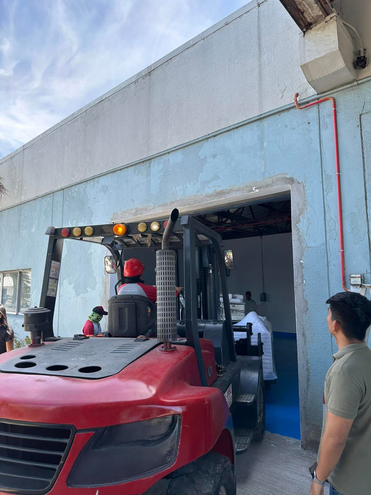 Red Forklift Loading White Bags Into a Blue Building, with People Watching — Kerubin Logistics Inc in the Philippines