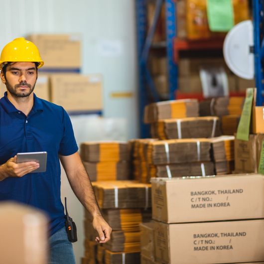 Warehouse worker in Yellow Hard Hat Using Tablet Near Stacked Boxes — Kerubin Logistics Inc in the Philippines