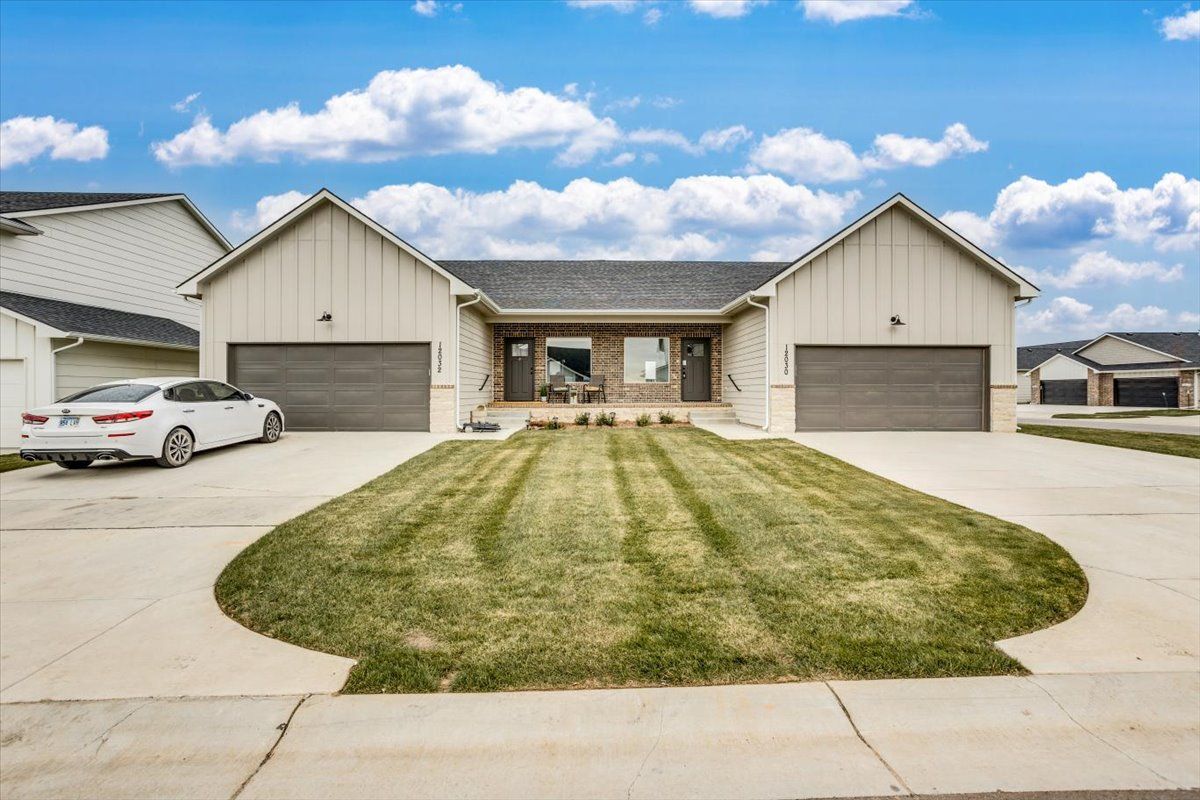 A white car is parked in front of a house with two garages.
