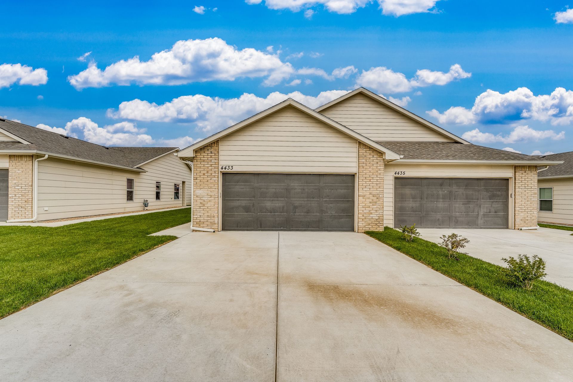A house with two garage doors and a concrete driveway in front of it.