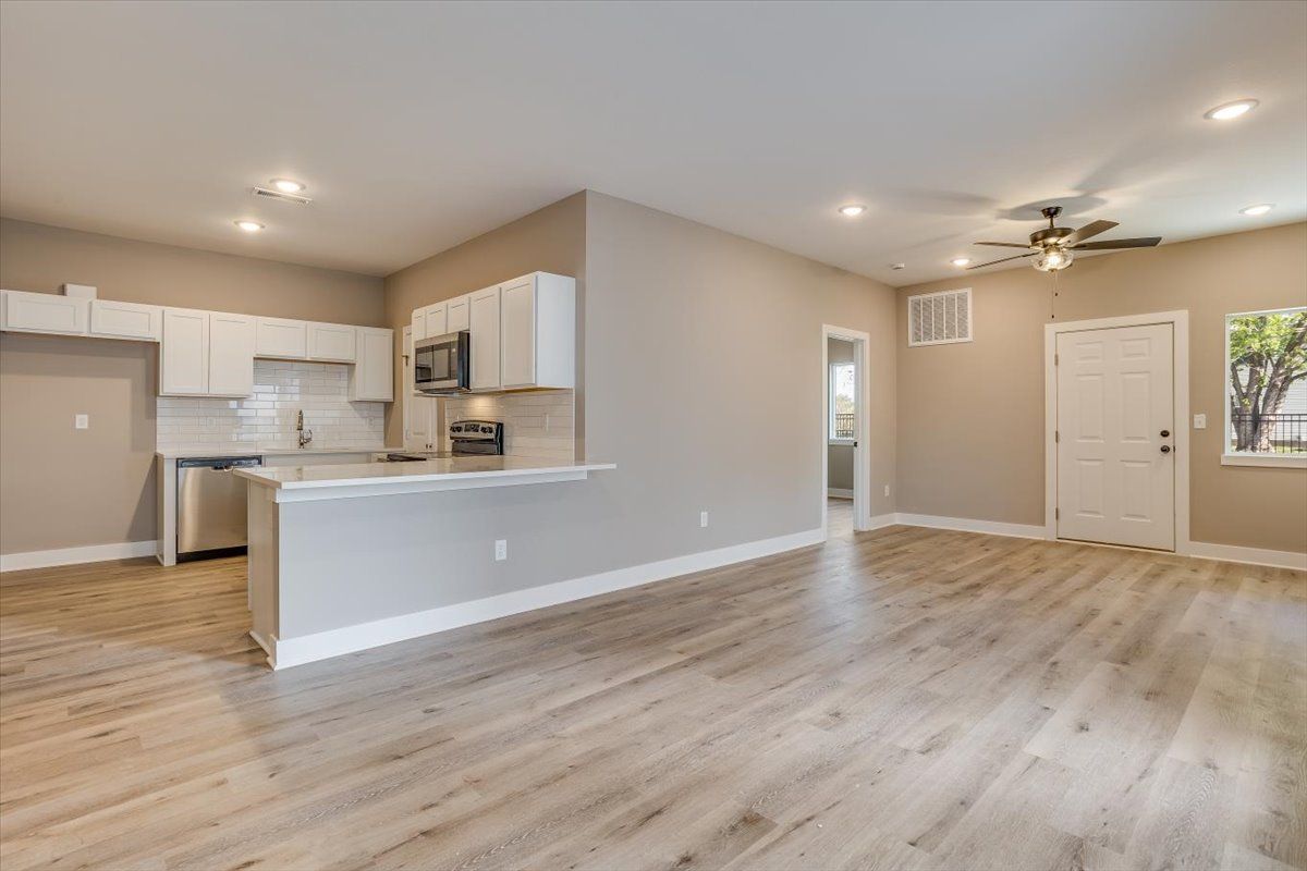 An empty living room with hardwood floors and a kitchen.