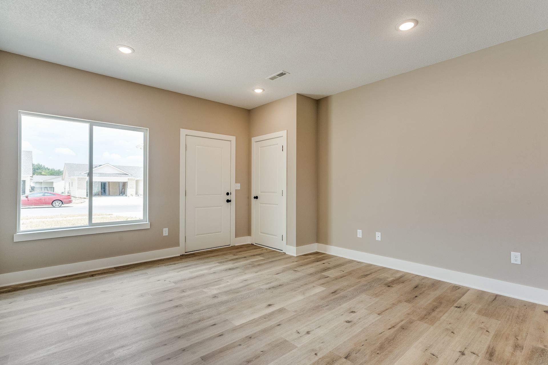 An empty living room with hardwood floors and two windows.