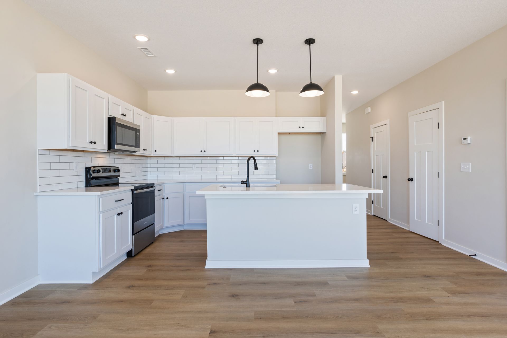 An empty kitchen with white cabinets , stainless steel appliances , and a large island.
