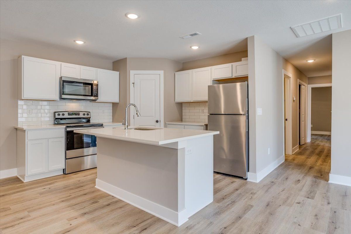 A kitchen with white cabinets , stainless steel appliances , and a large island.