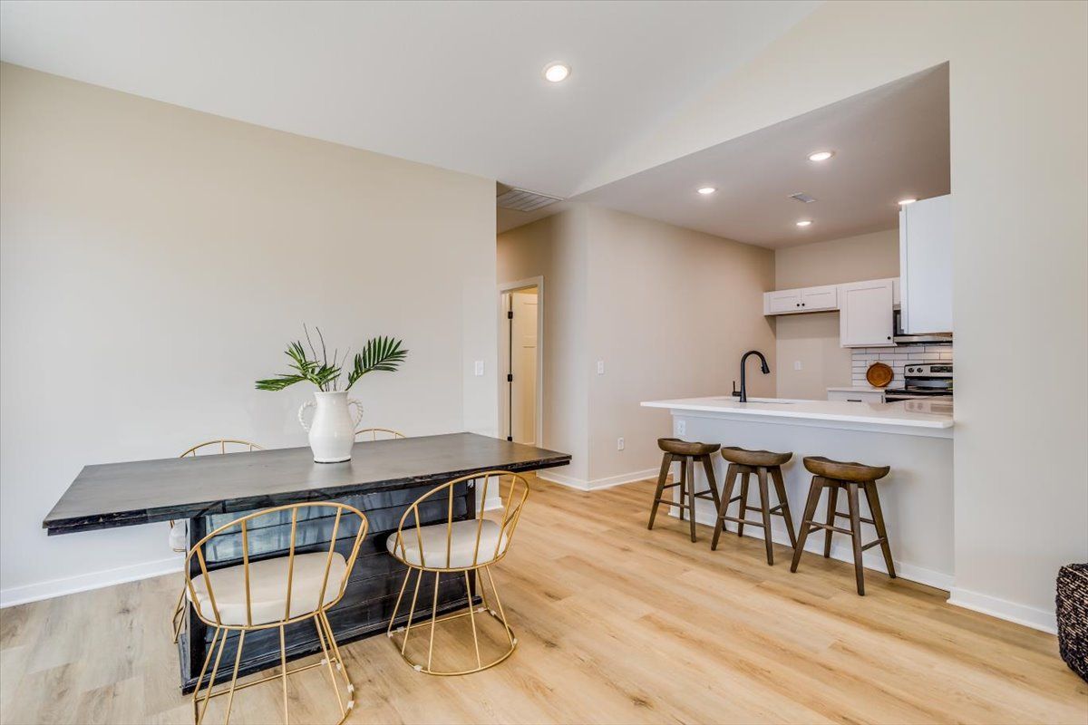 A dining room with a table and chairs and a kitchen in the background.