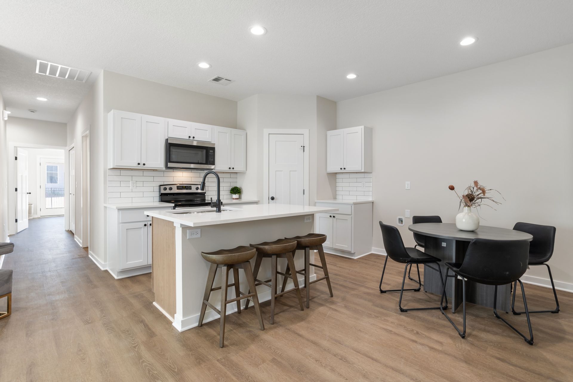 A kitchen and dining room in a house with hardwood floors and white cabinets.