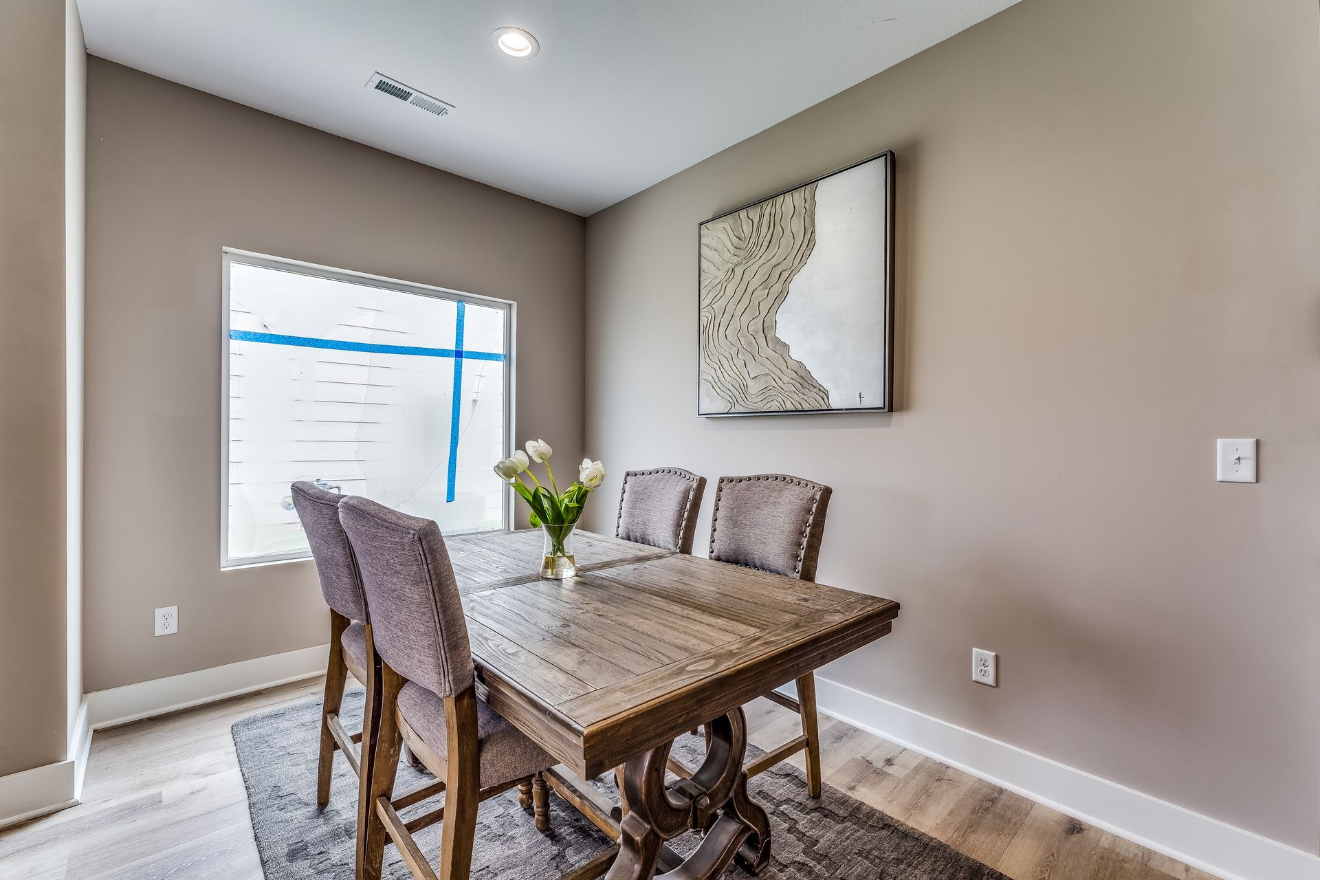 A dining room with a wooden table and chairs and a painting on the wall.