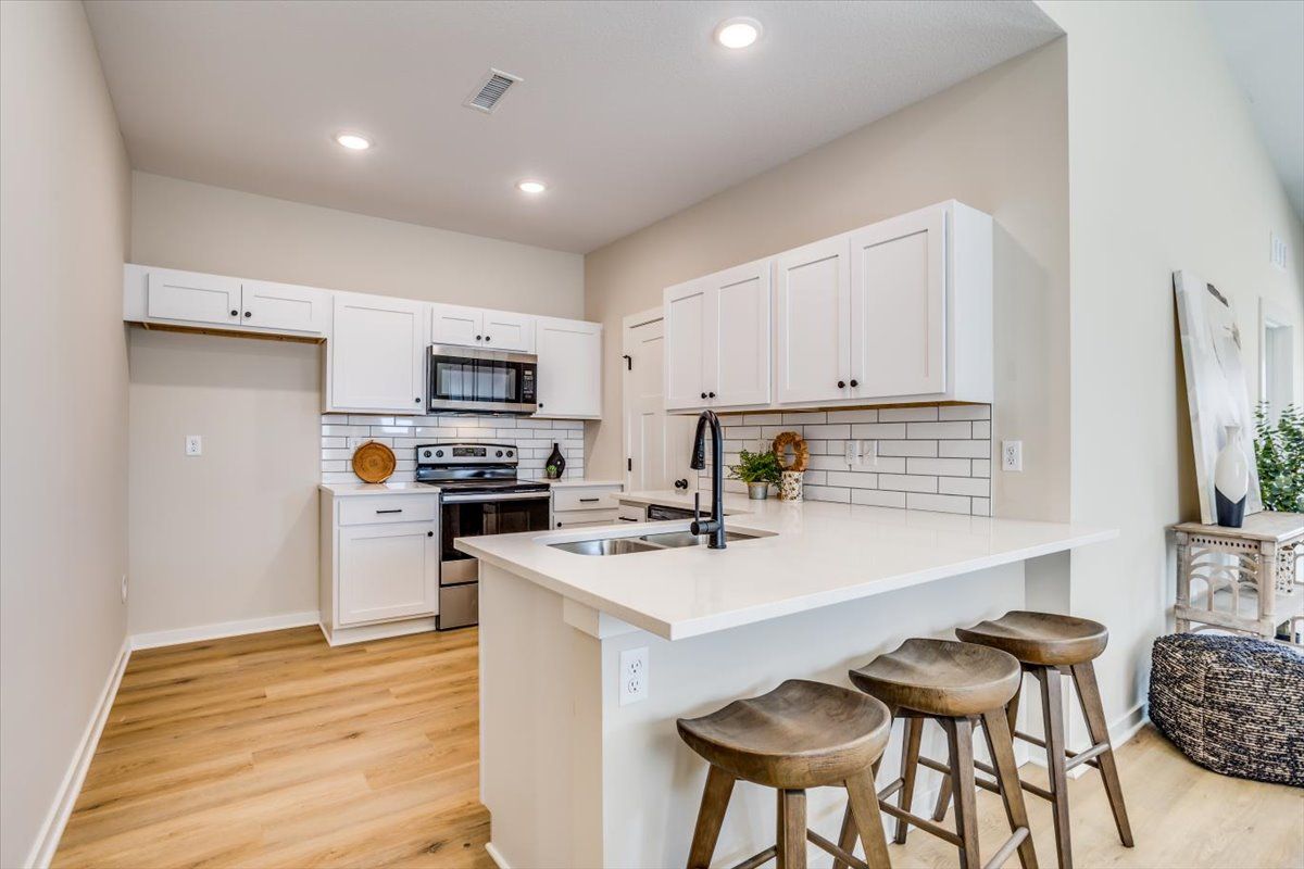 A kitchen with white cabinets , stools , a sink and a microwave.
