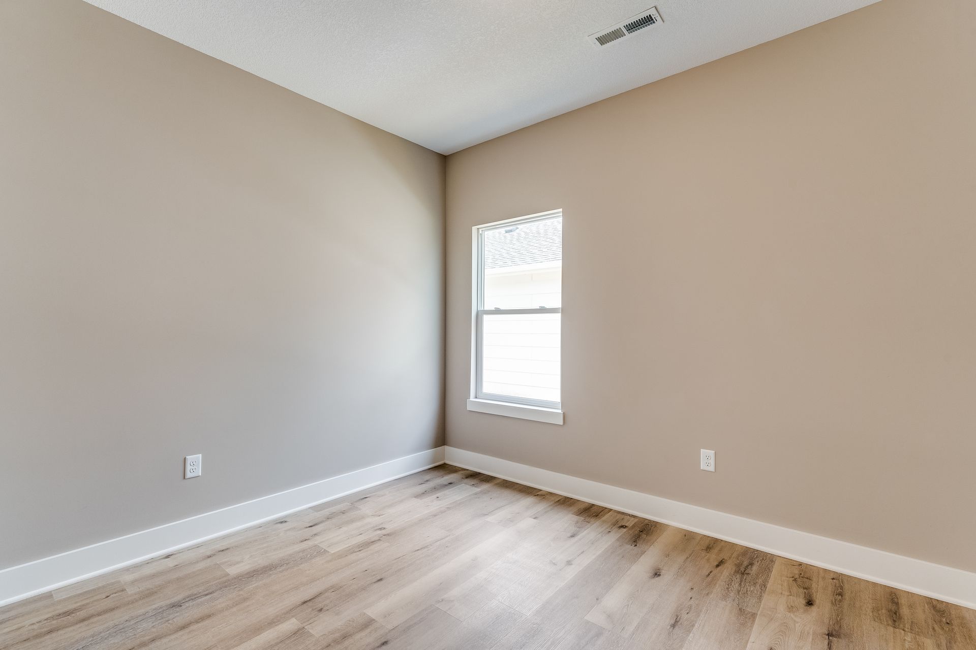 An empty bedroom with hardwood floors and a window.
