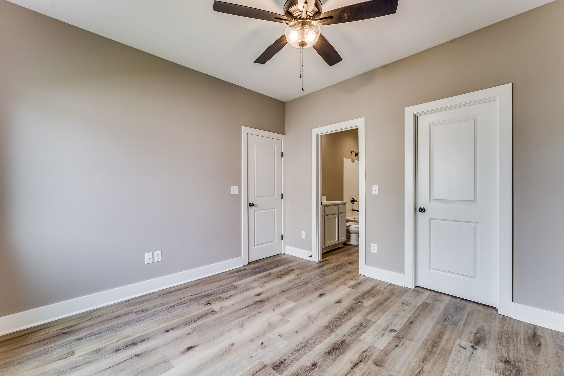 An empty bedroom with hardwood floors and a ceiling fan.