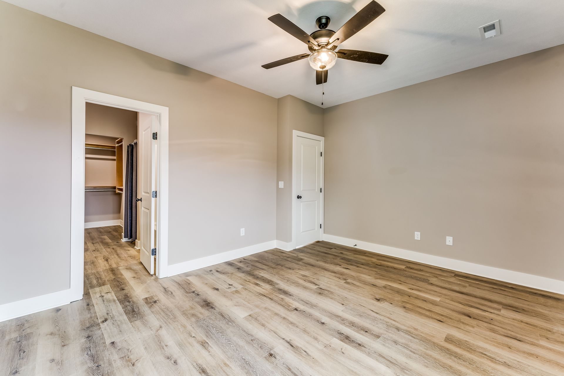An empty bedroom with hardwood floors and a ceiling fan.