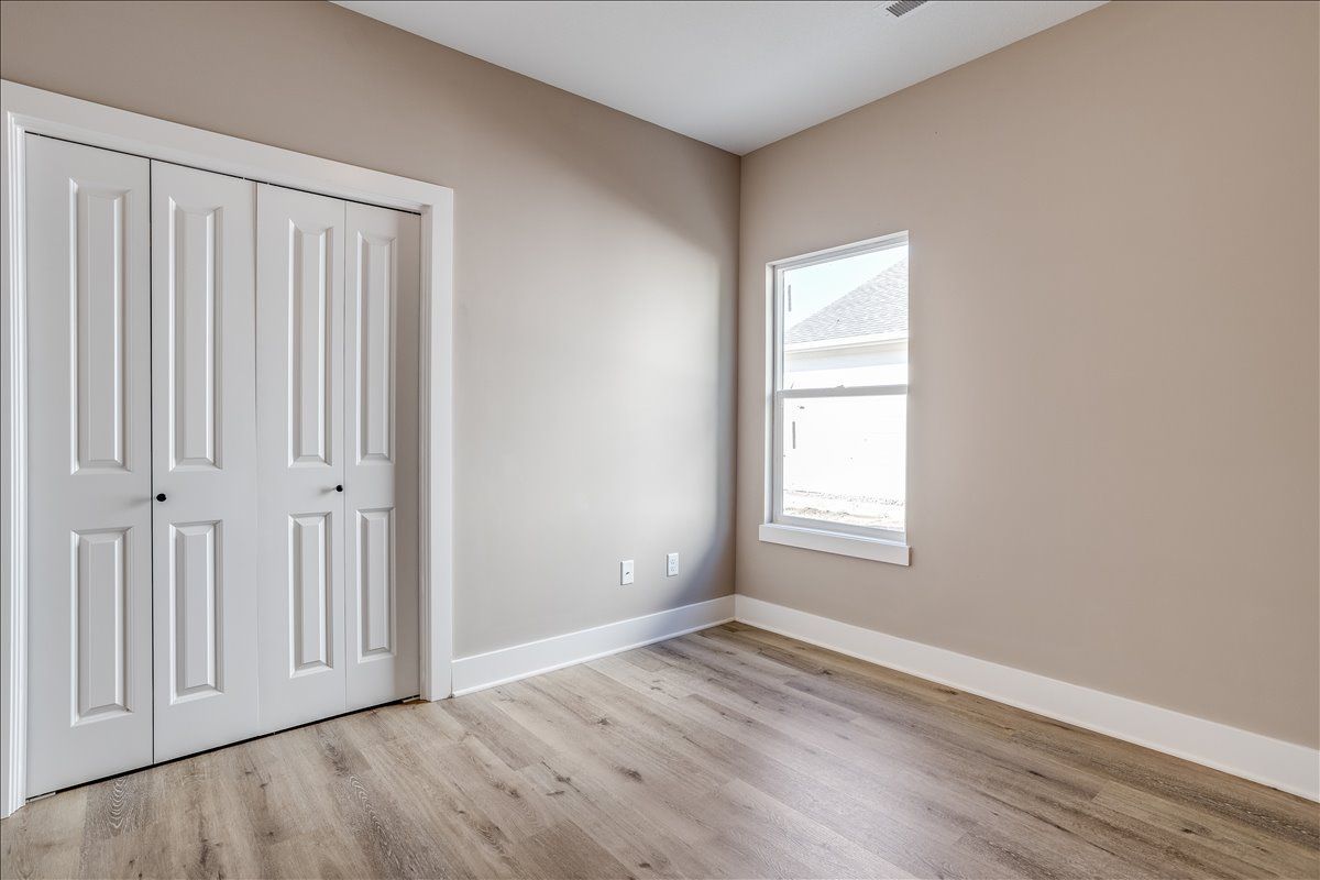 An empty bedroom with hardwood floors and a window.