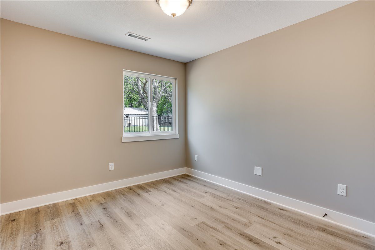 An empty bedroom with hardwood floors and a window.
