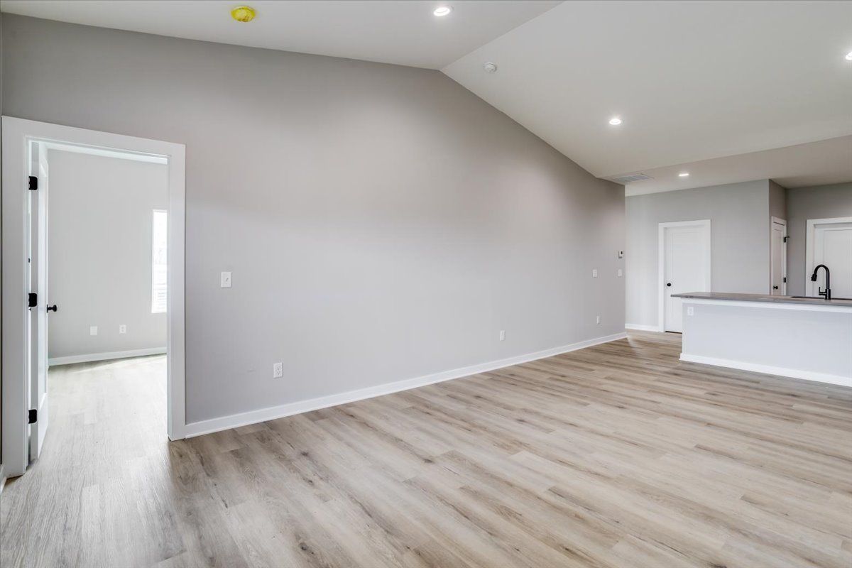 An empty living room with hardwood floors and a vaulted ceiling.