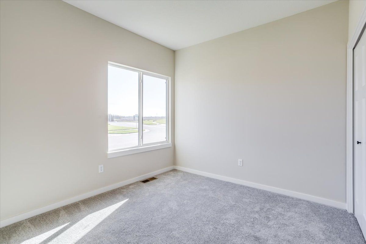 An empty bedroom with a carpeted floor and two windows.