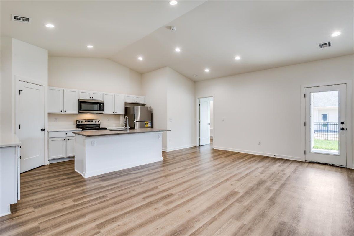 A large empty room with hardwood floors and a kitchen.