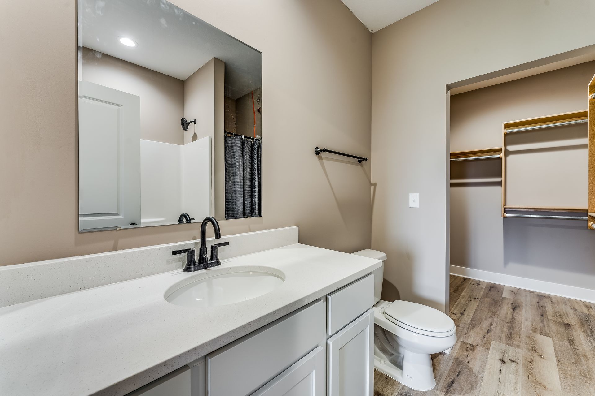 A bathroom with a sink , toilet , mirror and walk in closet.