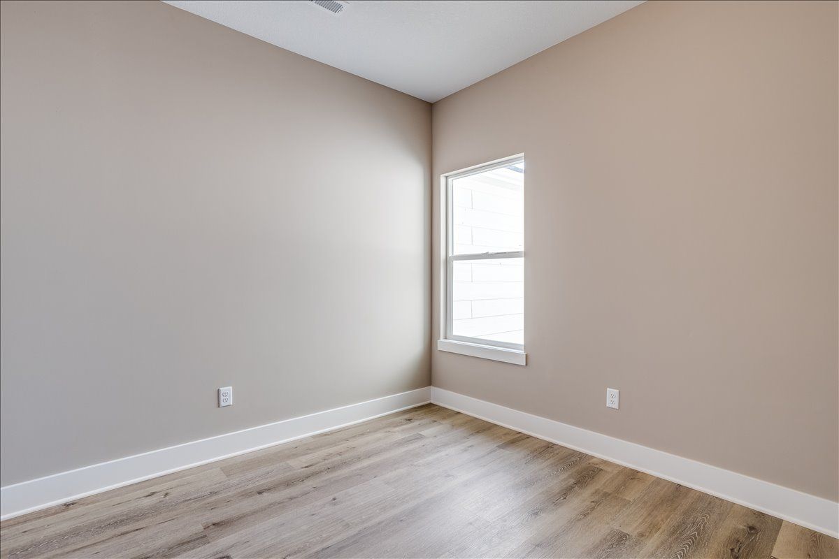 An empty room with a window and hardwood floors.