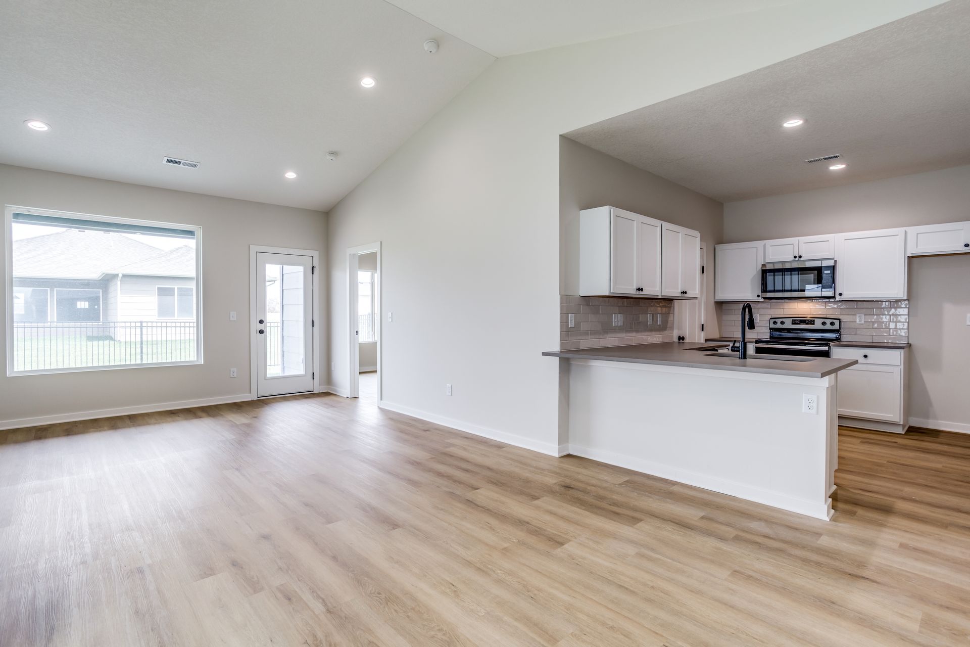 An empty living room with hardwood floors and a kitchen.