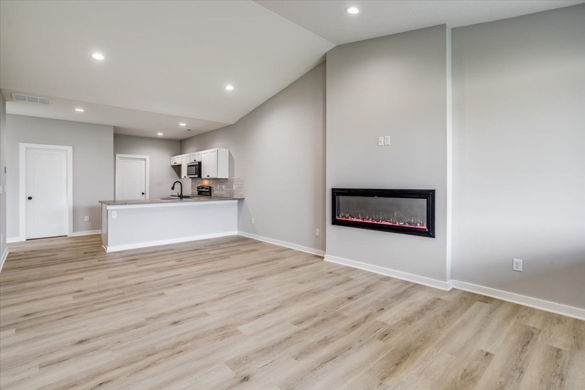 A living room with a fireplace and a kitchen in the background.