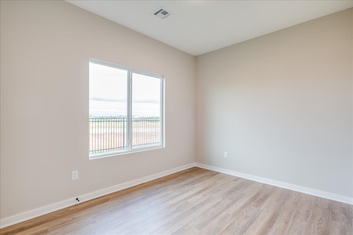 An empty bedroom with hardwood floors and two windows.