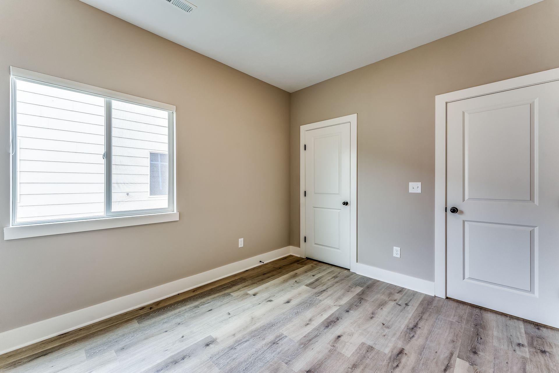 An empty bedroom with hardwood floors and two windows.