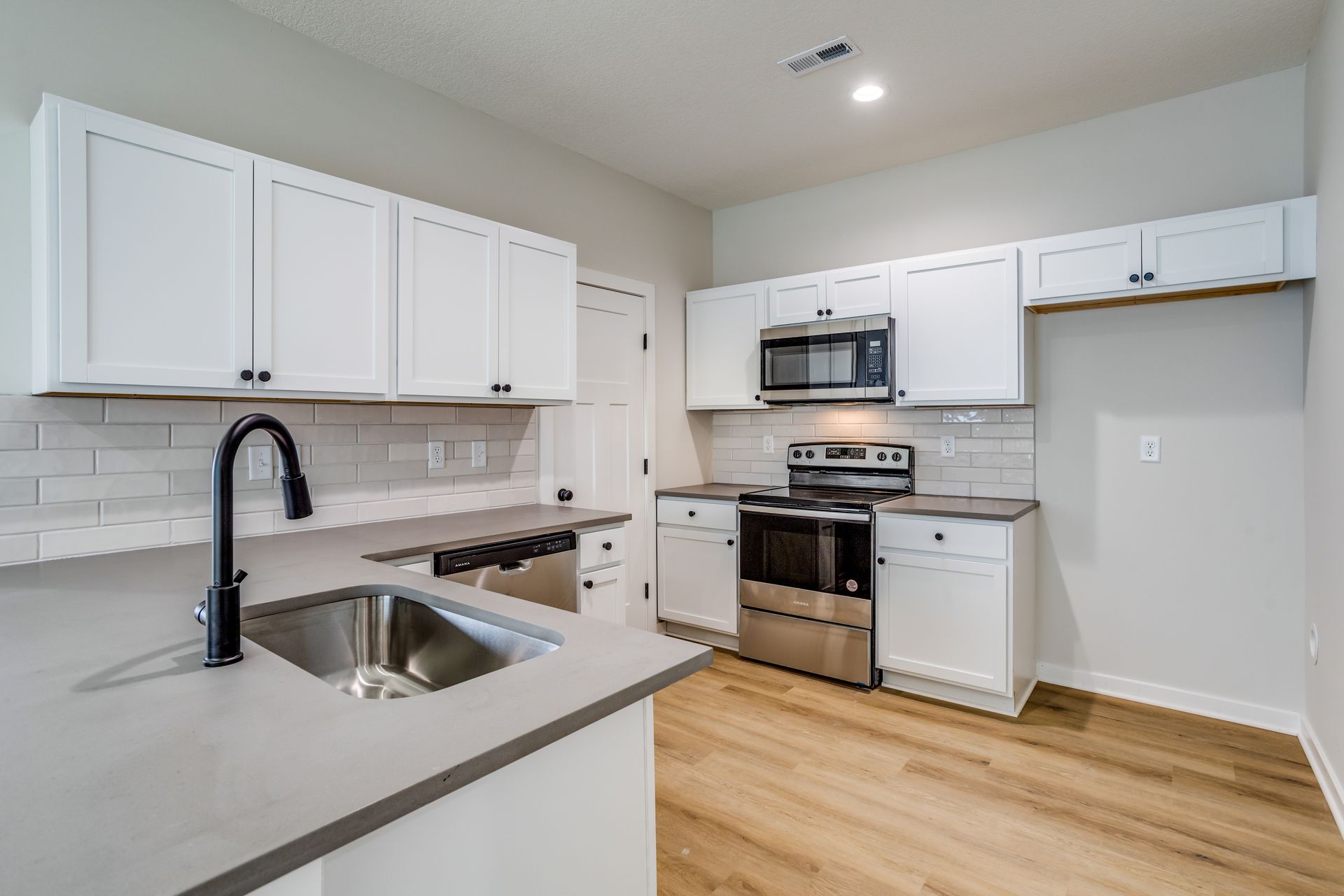 A kitchen with white cabinets , stainless steel appliances , a sink , and a microwave.