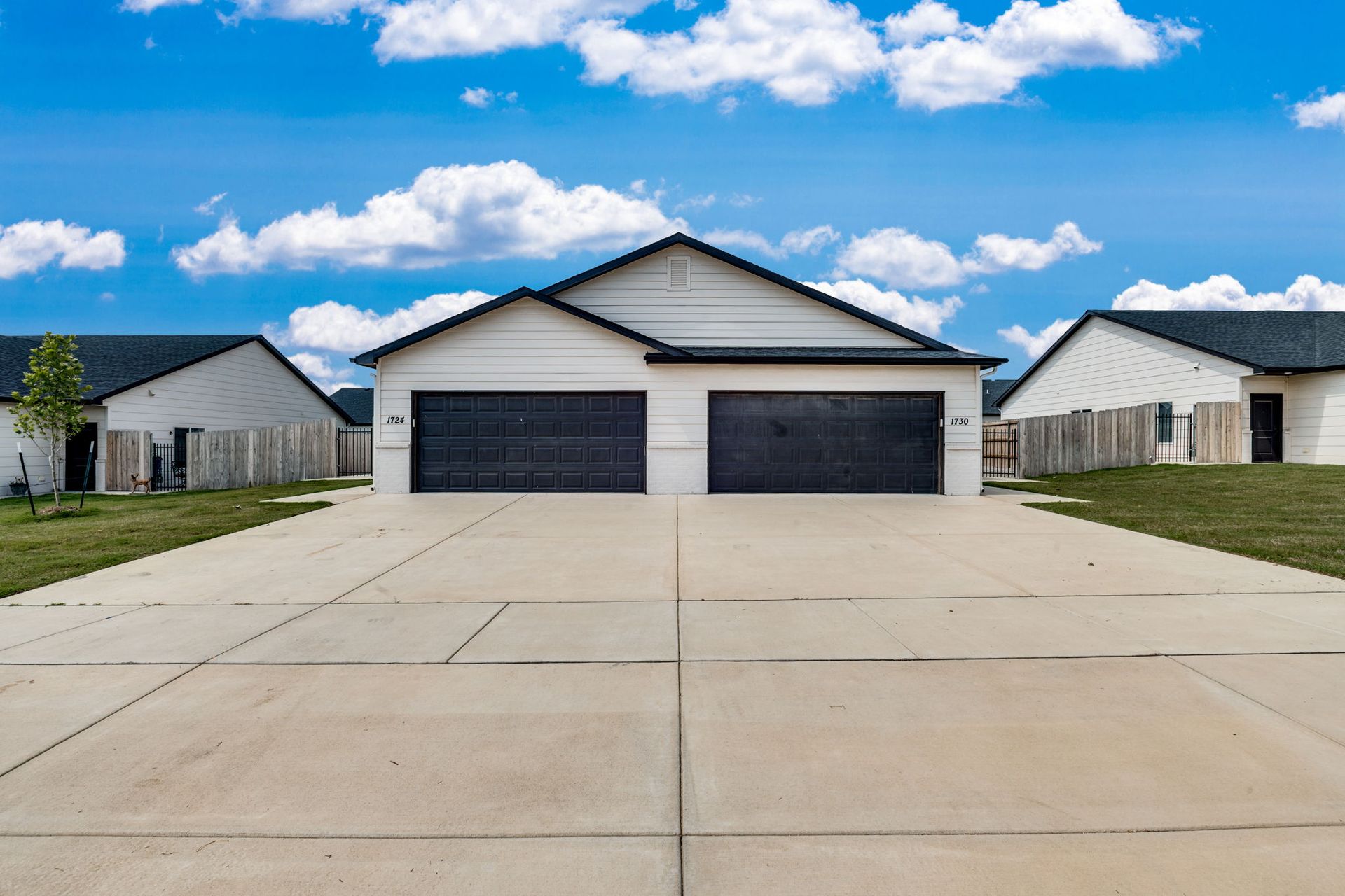 A white house with two garage doors and a concrete driveway in front of it.