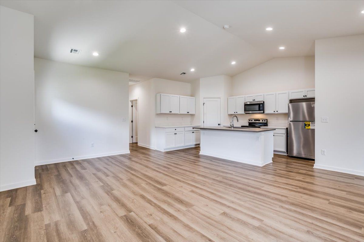 A living room with hardwood floors and a kitchen with stainless steel appliances.