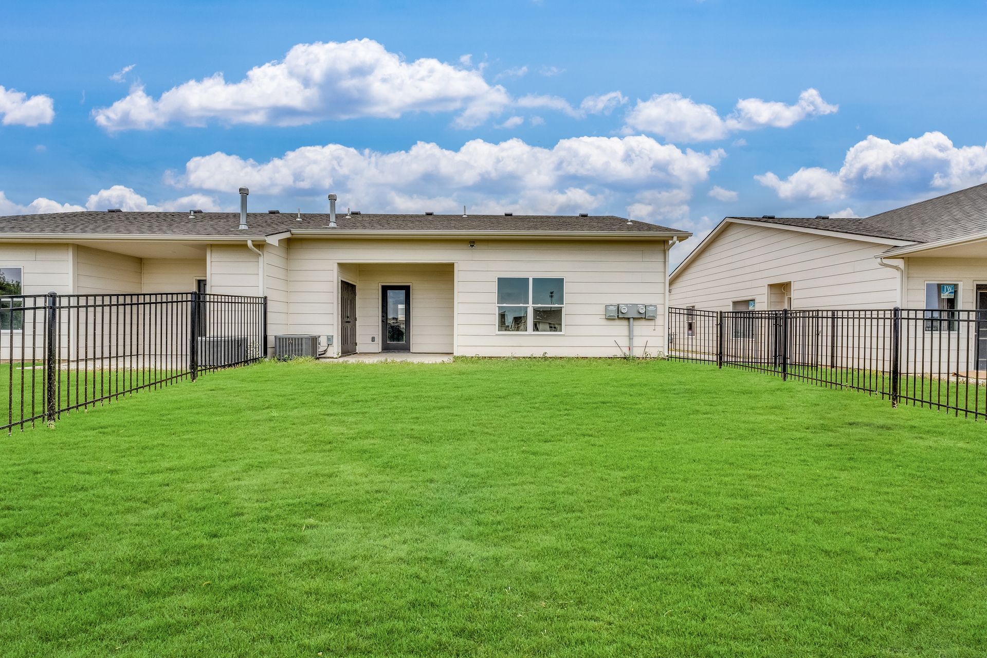 A large lawn in front of a house with a fence around it.