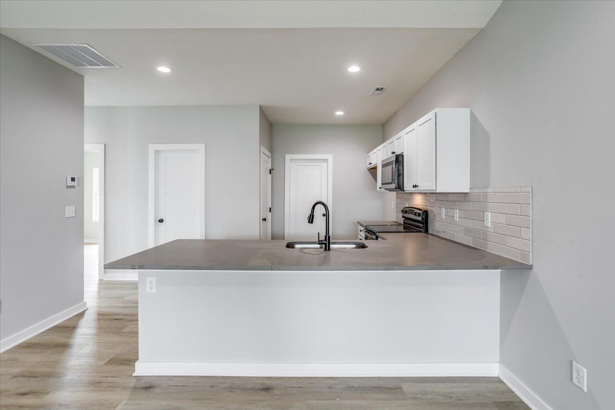 A kitchen with white cabinets , a sink , and a microwave.
