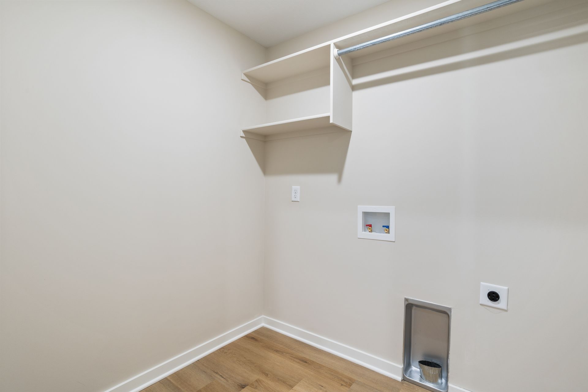 An empty laundry room with hardwood floors and shelves.