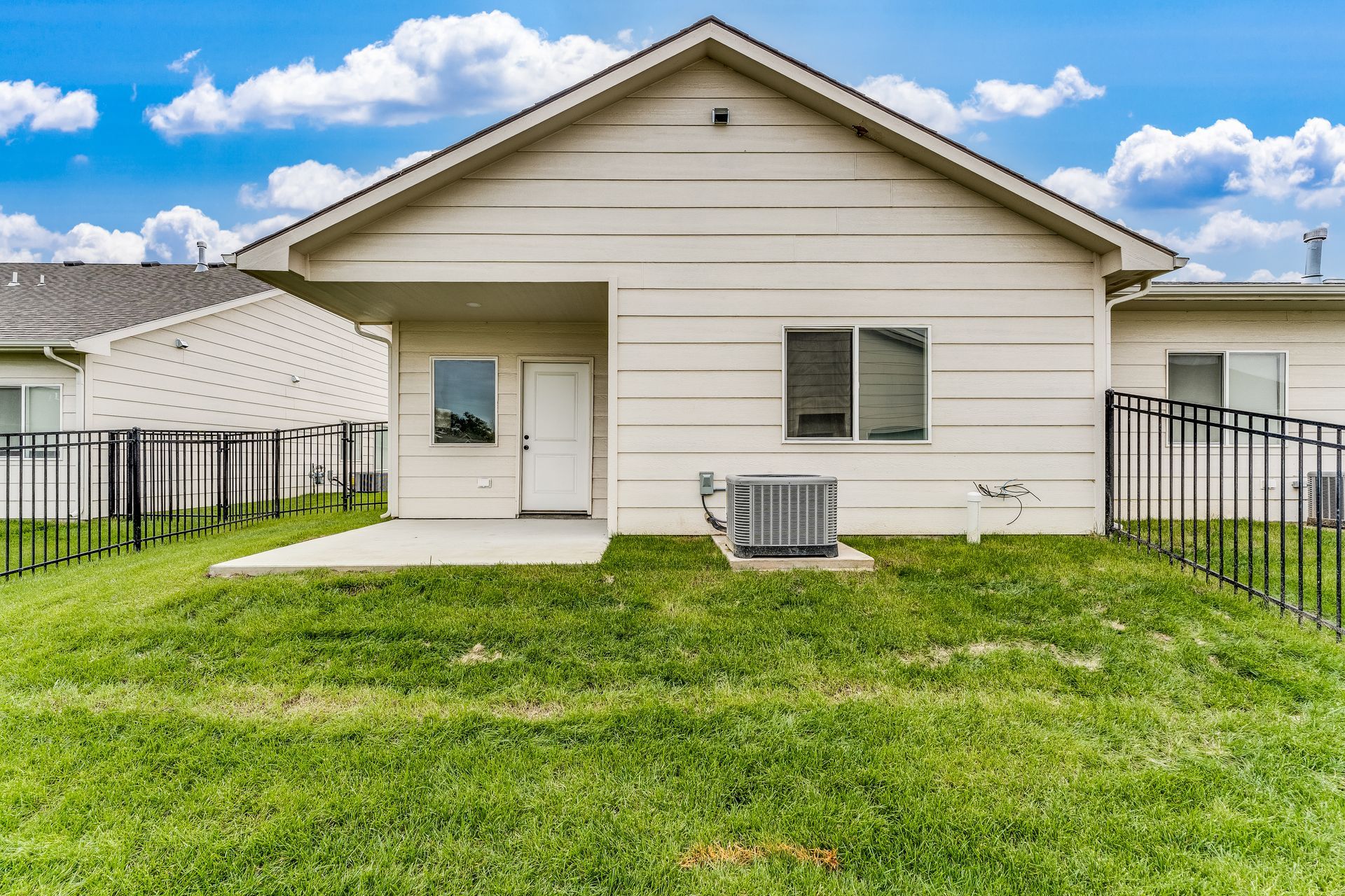 The back of a house with a fence and a lawn in front of it.