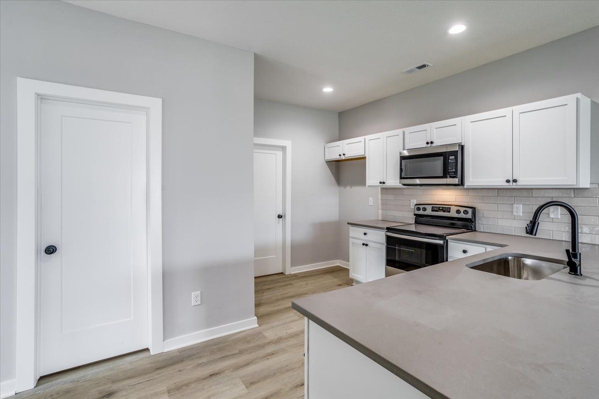 A kitchen with white cabinets , stainless steel appliances , a sink , and a microwave.