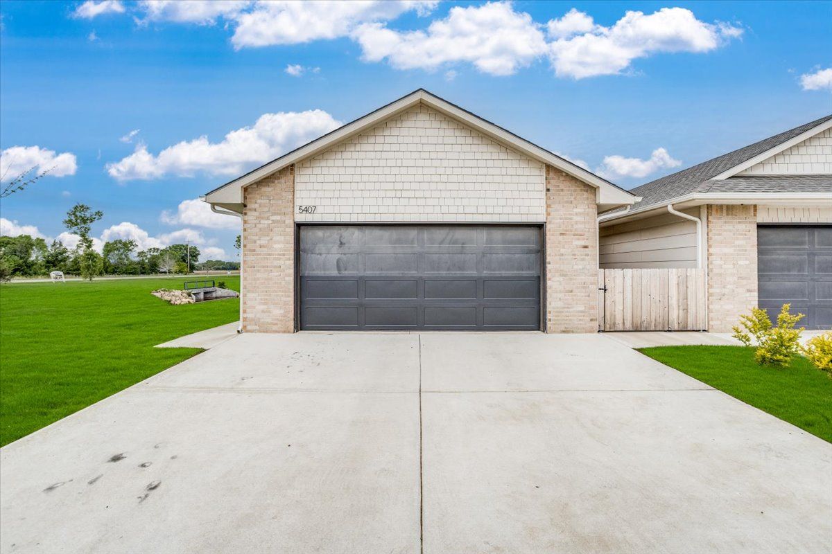A brick house with a gray garage door and a concrete driveway.