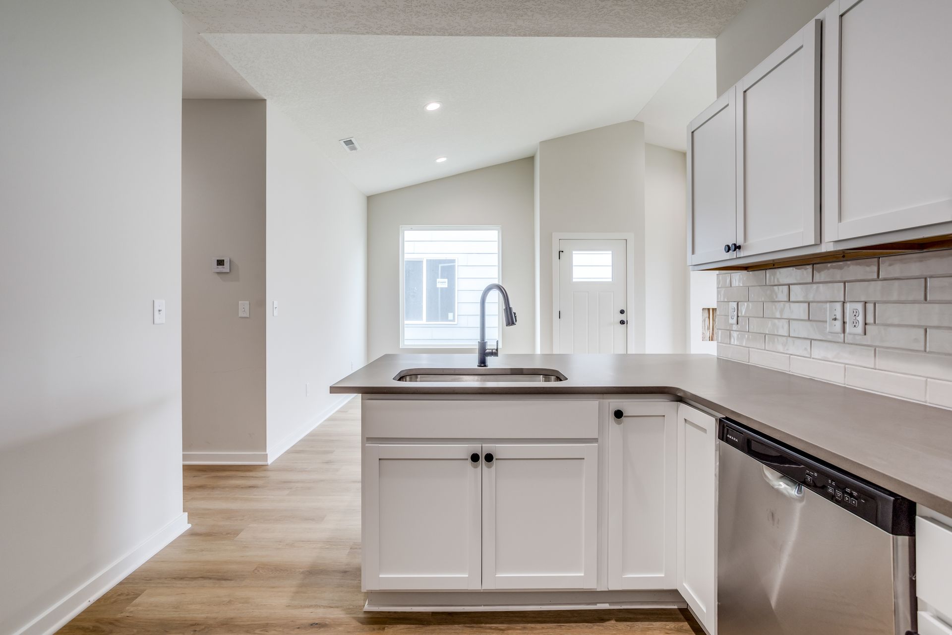 A kitchen with white cabinets , a sink , and a stainless steel dishwasher.