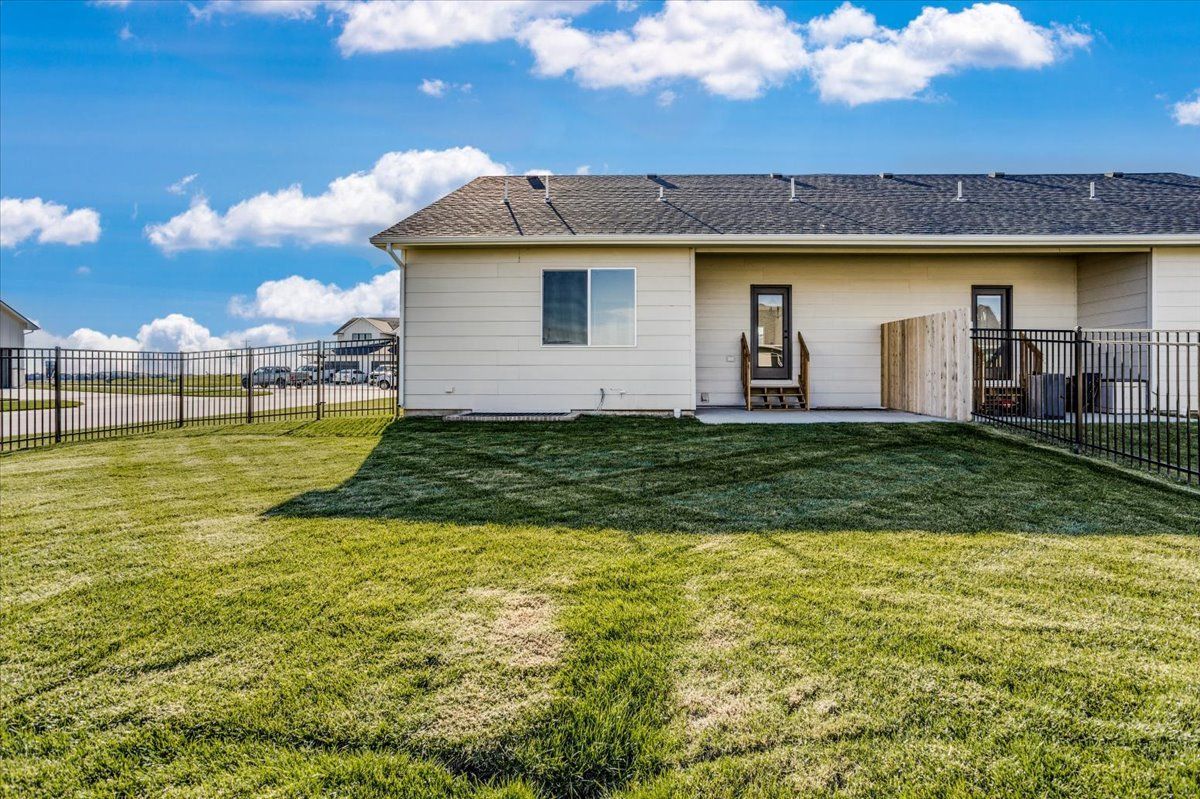 The backyard of a house with a large lawn and a fence.
