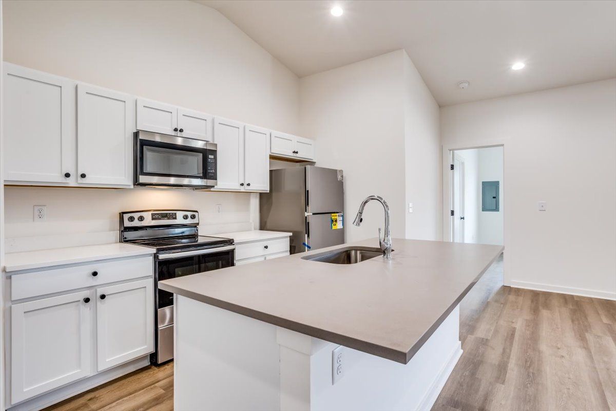 A kitchen with white cabinets , stainless steel appliances , a sink , and a refrigerator.