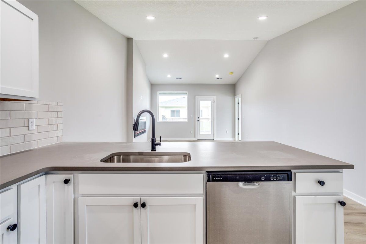 A kitchen with white cabinets , a sink , and a stainless steel dishwasher.