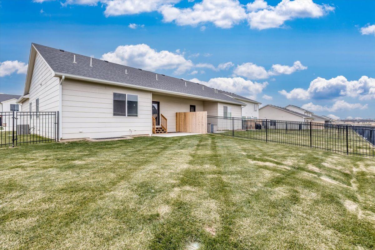 The backyard of a house with a fence and a lush green lawn.