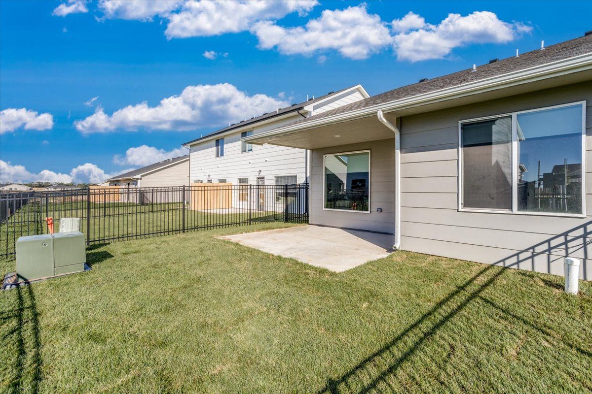 The backyard of a house with a large lawn and a fence.