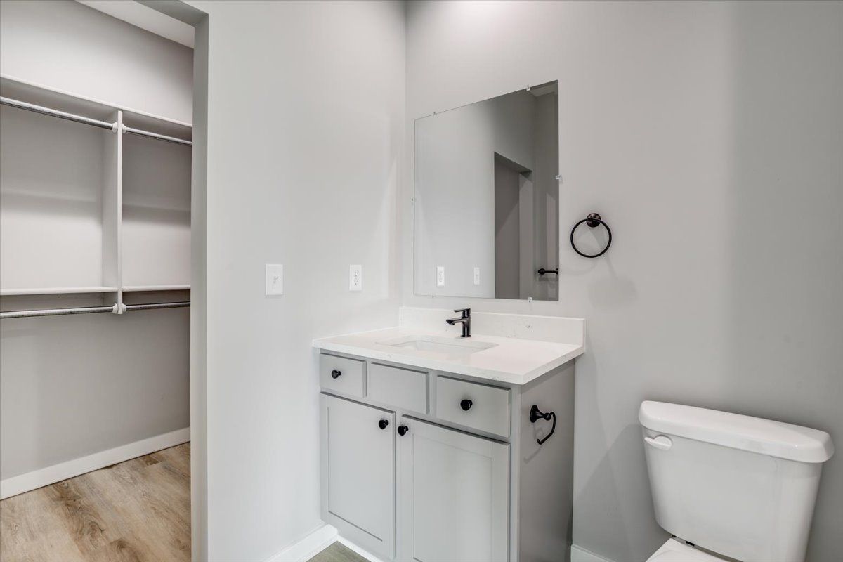 A bathroom with a sink , toilet , mirror and walk in closet.