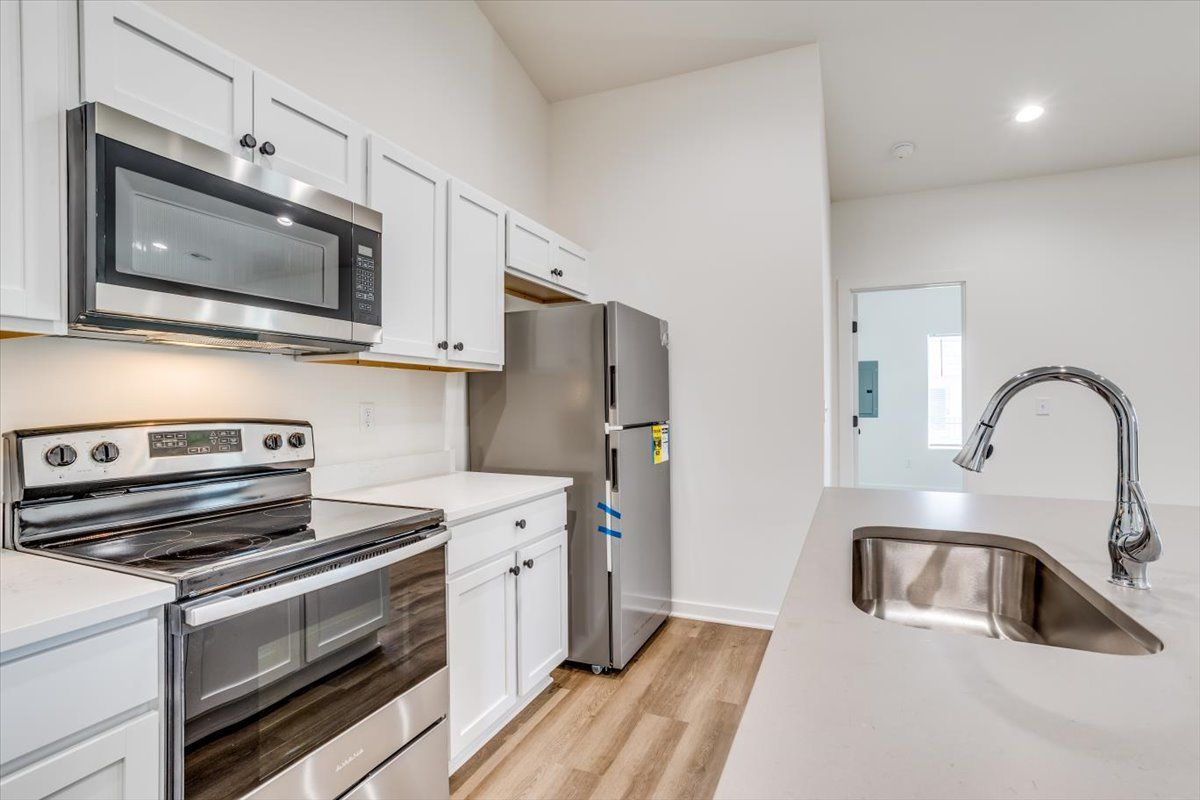 A kitchen with a stove , refrigerator , microwave and sink.