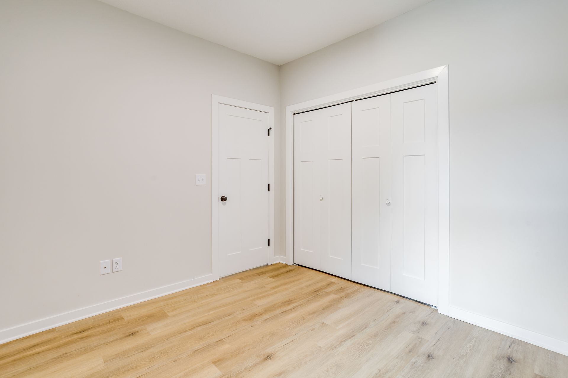 An empty bedroom with hardwood floors and white walls.