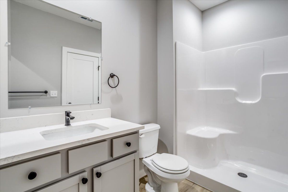 A bathroom with a toilet , sink , mirror and shower.