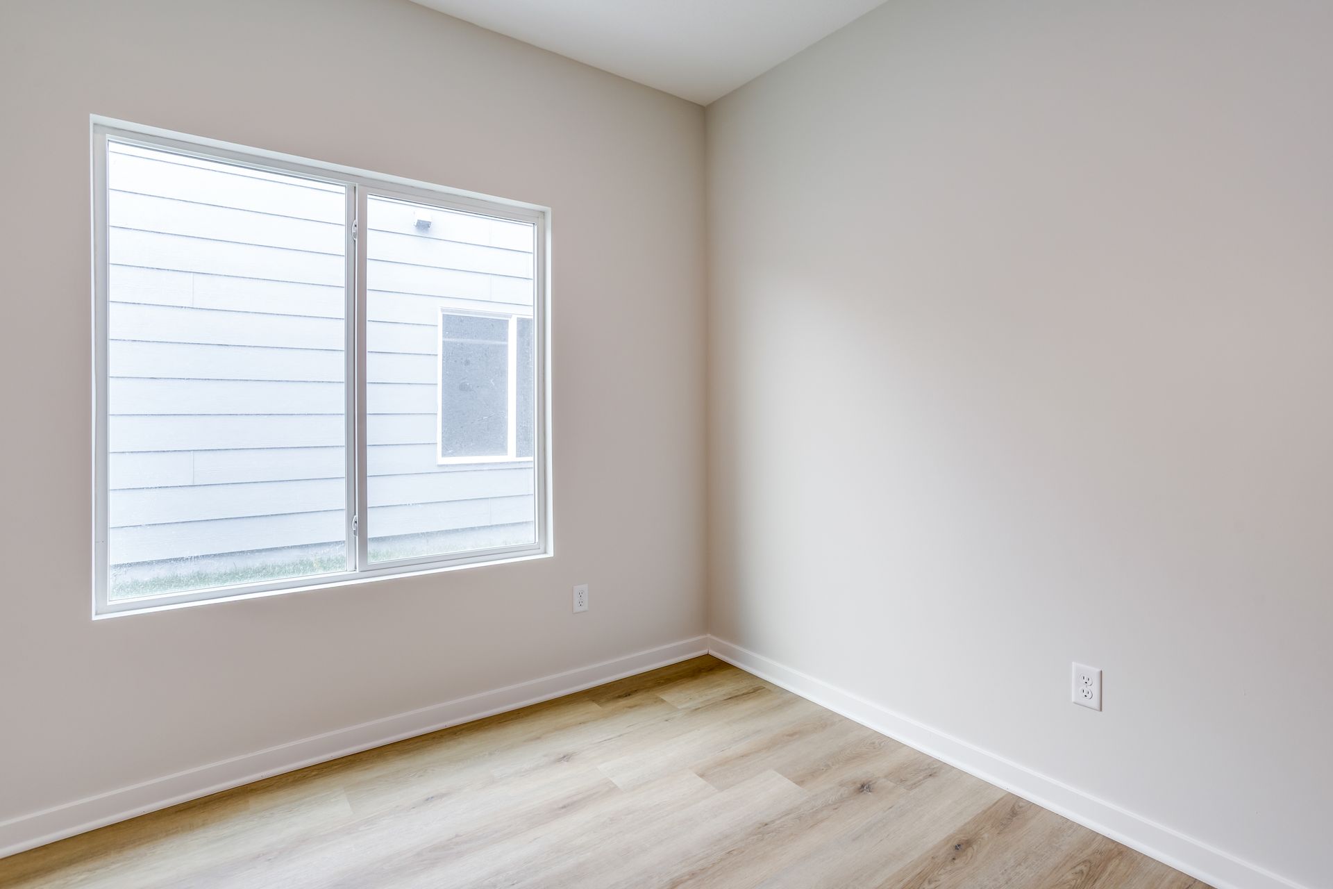 An empty room with a window and hardwood floors.