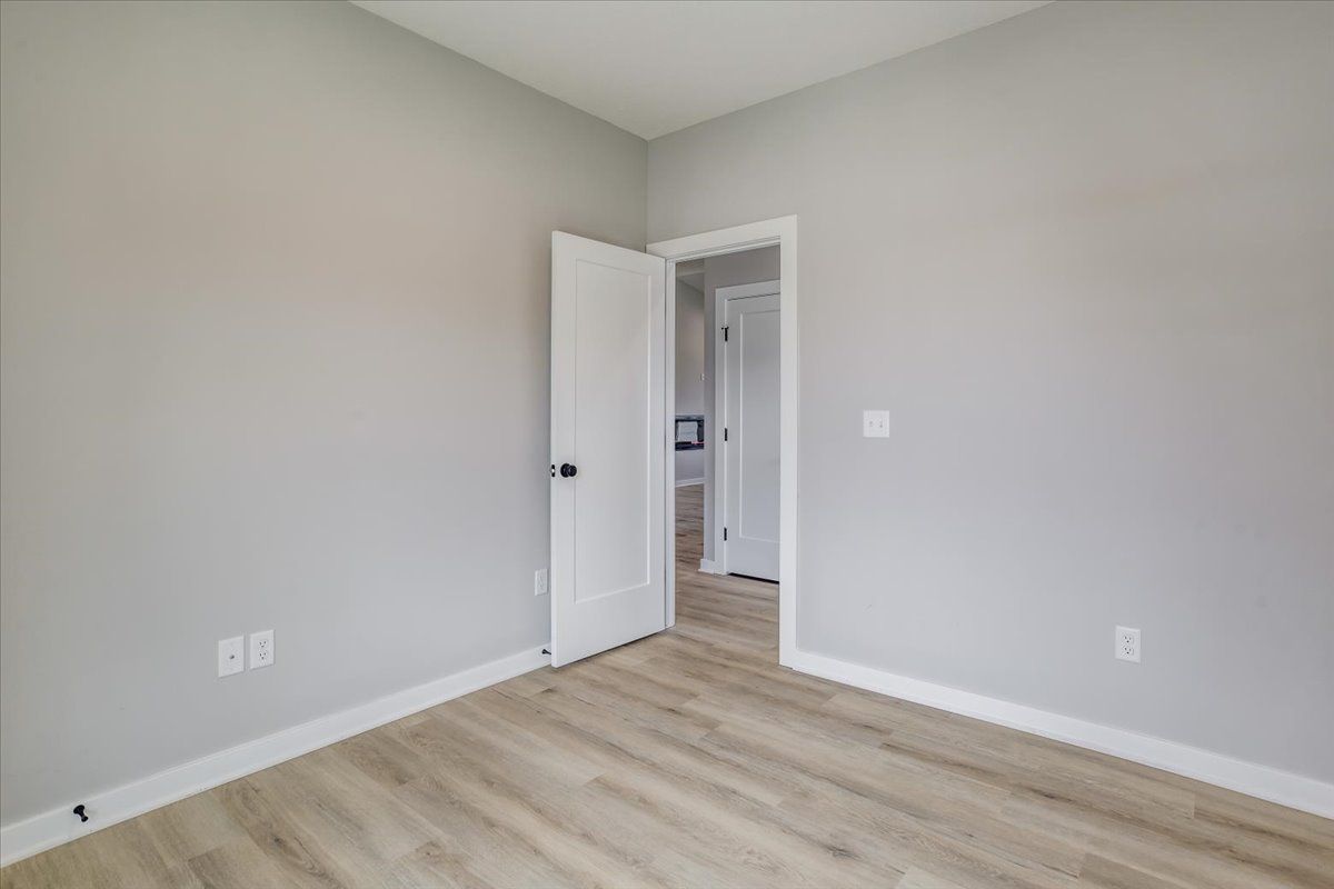 An empty bedroom with hardwood floors and gray walls.