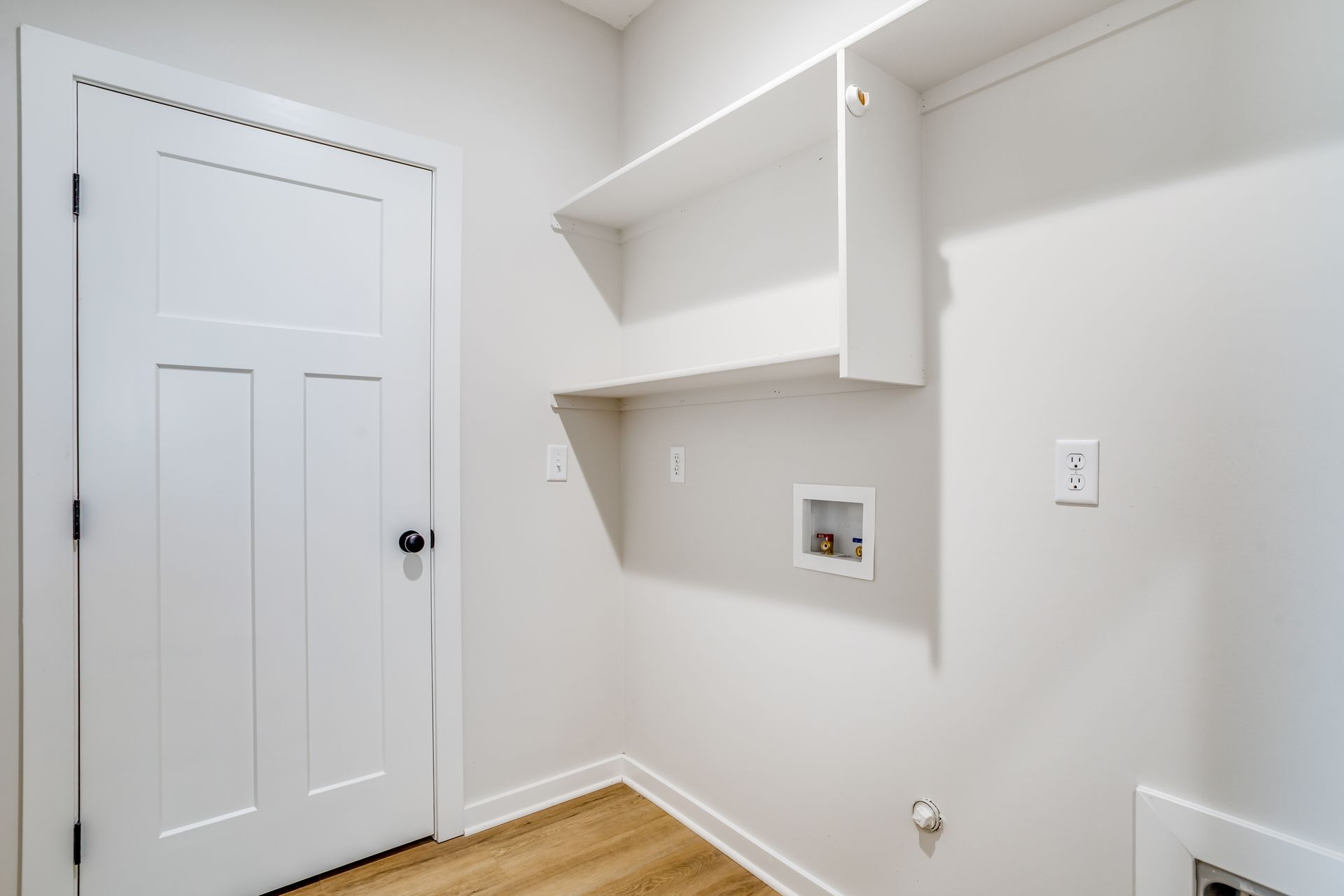 A laundry room with a door and a shelf on the wall.