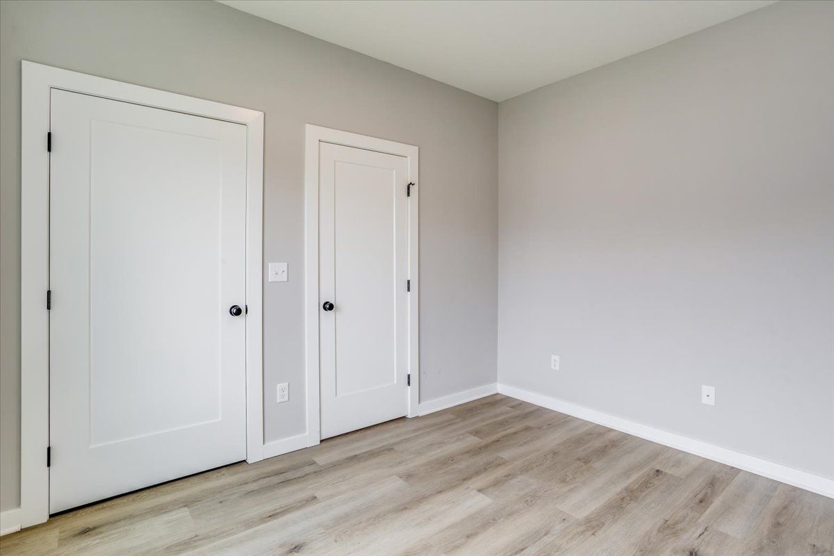 An empty room with two white doors and a wooden floor.